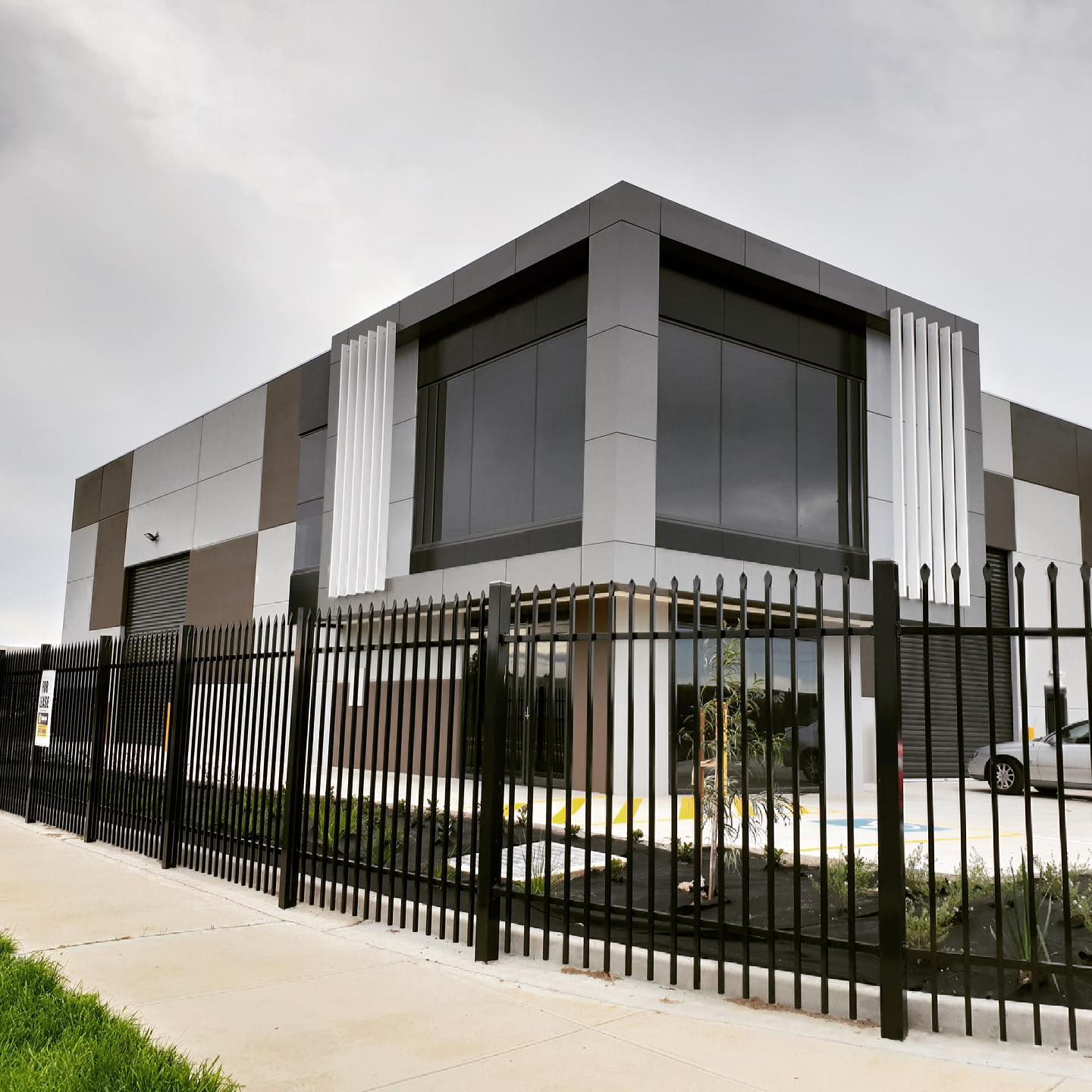 Modern grey and black Pamp Solutions warehouse building with large windows behind a black metal security fence.